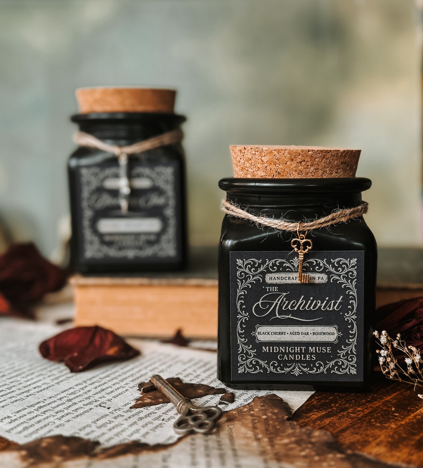 Black candle jar with cork lid and decorative label on a rustic surface with books and leaves.